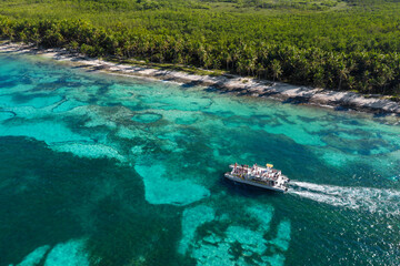 Fototapeta na wymiar Speed boat floating along tropical island with palm trees near caribbean sea. Dominican Republic. Aerial view