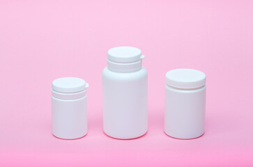 White different medecine or cosmetic jars on a pink background as a concept of cosmetology of medecine and treatment