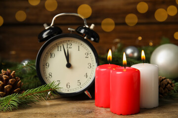 Alarm clock, burning candles and Christmas decor on wooden table, bokeh effect