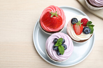 Sweet cupcakes with fresh berries on light wooden table, flat lay. Space for text