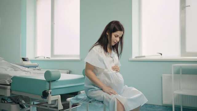 Caucasian pregnant woman breathing deeply during painful contractions at hospital ward. Young brunette preparing for labour at modern clinic. Pregnancy and health care concept.
