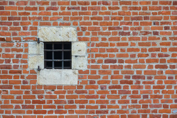 Fototapeta na wymiar The old red brick fortress wall. There is a square window with a stone frame and iron bars. Background. Texture.