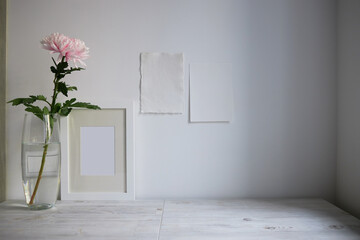 Scandinavian style. Interior Design. Large pink chrysanthemum in a long glass vase. Photo frame. Two blank sheets of paper on the wall. Empty space for text