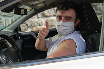 Portrait of a young man in a car showing the arm with the patch, after having been vaccinated against the Covid-19 Coronavirus in the hospital concourse