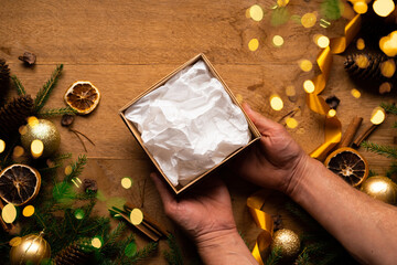 Male hands make a Christmas and New Year's gift on a wooden background branches of a Christmas tree, gold decorations, cinnamon sticks and orange. Christmas composition.