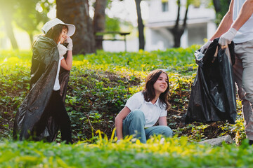 Volunteer team two girls and a man holding packets and gathering garbage outdoors, participate in a mission to clean up nature from garbage. © Viorel