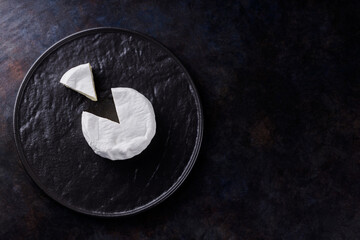 Camembert on a dark background. Soft cheese with white mold on a black plate. Minimalism. Copy space