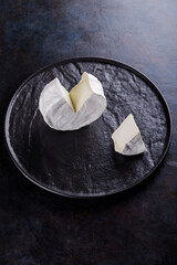 Camembert on a dark background. Soft cheese with white mold on a black plate. Minimalism. Copy space