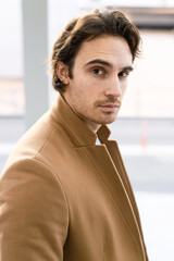 Portrait of brunette man in brown coat looking at camera outdoors 