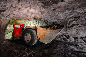 An underground loading machine carries a full bucket of ore. Special low-profile equipment for...