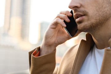 Cropped view of businessman in coat talking on cellphone outdoors in evening 