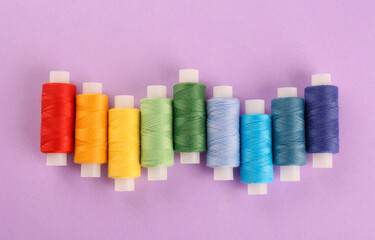 Different colorful sewing threads on lilac background, flat lay