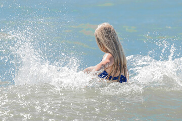 Young cheerful girl teenager blonde makes splashes of water with her hands in the sea