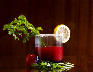 Bloody Mary cocktail in the glass. An alcoholic drink with a slice of lemon a sprigs of celery and cherry tomato at the dark polished table. Landscape orientation image in the dark key style.