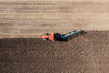 Tractor pulling plow in agricultural field on sunny day, aerial view