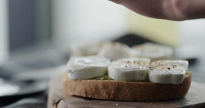 Slow motion add spices on on fresh ciabatta slice with pesto and mozzarella to make sandwich closeup