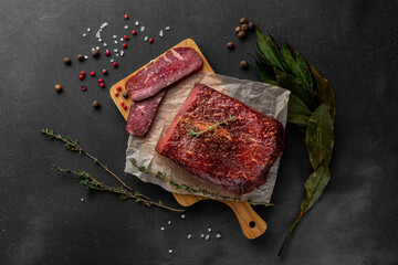 still life composition with a piece of red smoked dry ham on a wooden cutting board, top view