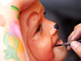 the process of drawing a child's face on a holiday. a little boy is painted with a brush on his face in the form of a hamster. Birthday