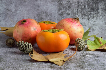 Autumn fruit, persimmon and pomegranate, leaves and pineapples on scattered outline and stone background. Copy space.