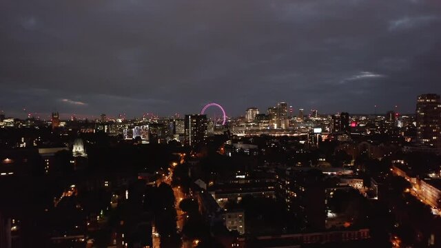 Descending shot of night cityscape. Urban neighbourhood at night. Illuminated London Eye in distance. London, UK