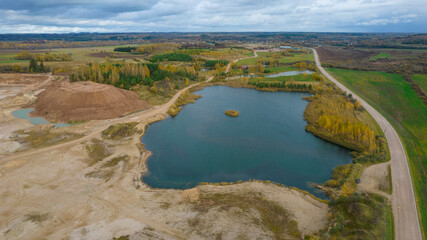 Open pit gravel mining. Little lake or pond of unusual shape with a beautiful autumn nature and gravel piles photographed from above with a drone. Real is beautiful 