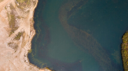 Little lake or pond of unusual shape with a beautiful autumn nature, small house and gravel road photographed from above with a drone. Real is beautiful 