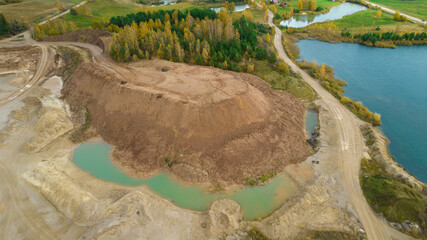 Open pit gravel mining. Little lake or pond of unusual shape with a beautiful autumn nature and gravel piles photographed from above with a drone. Real is beautiful 