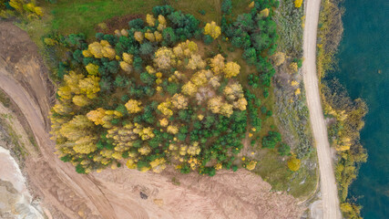 Little lake or pond of unusual shape with a beautiful autumn nature, small house and gravel road photographed from above with a drone. Real is beautiful 