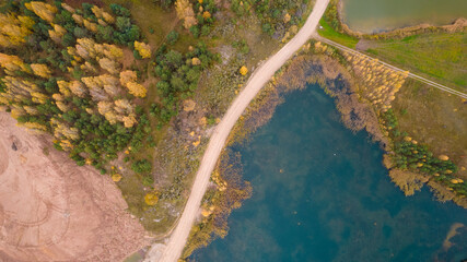 Little lake or pond of unusual shape with a beautiful autumn nature, small house and gravel road photographed from above with a drone. Real is beautiful 