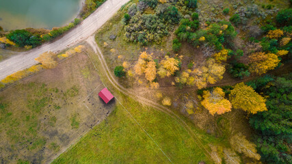Little lake or pond of unusual shape with a beautiful autumn nature, small house and gravel road photographed from above with a drone. Real is beautiful 