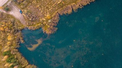 Little lake or pond of unusual shape with a beautiful autumn nature and mud road photographed from above with a drone. Real is beautiful 