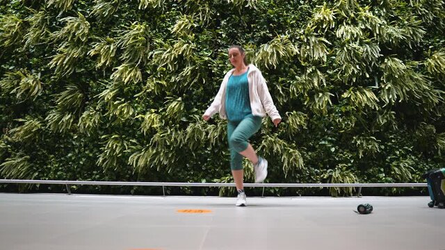 Girl dancing shuffle at the airport against a wall of plants