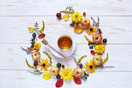 Apples, flowers and honey with copy space form a floral decoration. Concept  for Rosh Hashanah the Jewish New Year, harvest festival, Lammas. Top view, close up on white  wooden background.
