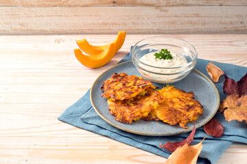 Squash potato fritters or pancakes with a curd cream dip on a blue plate and a wooden table, vegetarian autumn meal, copy space, selected focus