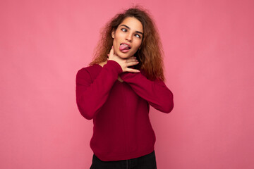 Portrait of young emotional beautiful brunette curly woman with sincere emotions wearing trendy pink pullover isolated on pink background with copy space and keeping hands on neck and strangling