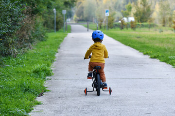 Child cycling on a bike path in the forest. Kid wearing a blue helmet and riding a bike with training wheels.