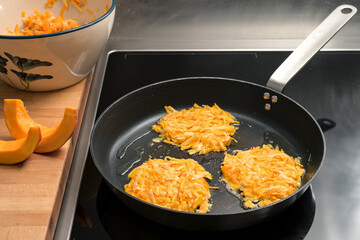 Cooking hash browns from potato and red kuri squash in a black pan, also called fried pumpkin rosti...