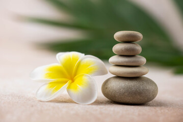 Fototapeta na wymiar Pyramids of gray and white zen pebble meditation stones on beige background with plumeria tropical flower. Concept of harmony, balance and meditation, spa, massage, relax