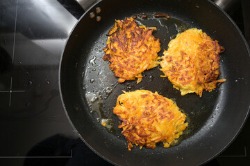 Golden roasted vegetable fritters from potato and red kuri squash in a black pan, also called pumpkin rosti or autumn pancake, copy space, high angle view from above