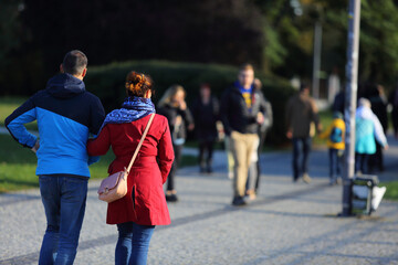 Para młodych ludzie, kobieta i mężczyzna spaceruje deptakiem, chodnikiem w parku.	