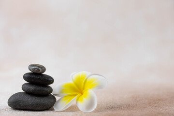 Fototapeta na wymiar Pyramids of gray and white zen pebble meditation stones on beige background with plumeria tropical flower. Concept of harmony, balance and meditation, spa, massage, relax