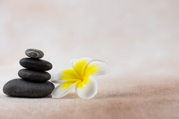 Pyramids of gray and white zen pebble meditation stones on beige background with plumeria tropical...