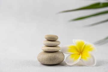 Obraz na płótnie Canvas Pyramids of gray and white zen pebble meditation stones on white background with plumeria tropical flower. Concept of harmony, balance and meditation, spa, massage, relax