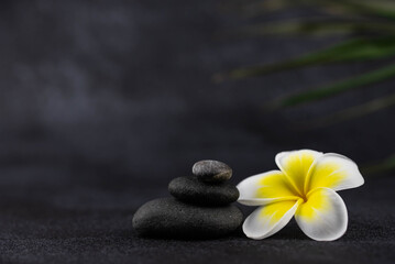 Obraz na płótnie Canvas Pyramids of gray and white zen pebble meditation stones on black background with plumeria tropical flower. Concept of harmony, balance and meditation, spa, massage, relax