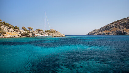 Yacht on anchor in turquoise sea water between rocky seashore islands