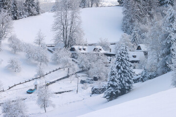 A hamlet of houses under the snow. Wooden houses in a hollow in the mountain are covered with snow. Only the windows stand out.