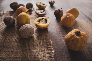 Fototapeta na wymiar Quince fruits and walnut on wooden table. Autumn harvest concept. Autumn rustic still life. Wild quince apples with seeds and nuts. Ripe organic food. Seasonal dessert.