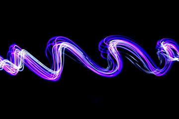Long exposure photograph of neon pink and purple colour in an abstract swirl, parallel lines pattern against a black background. Light painting photography.