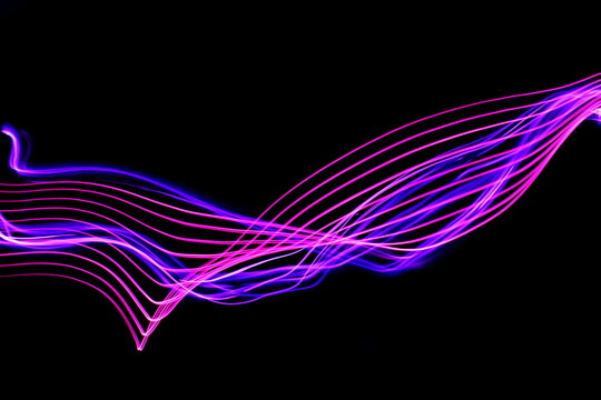 Long exposure photograph of neon colour in an abstract swirl, parallel lines pattern against a black background. Light painting photography.
