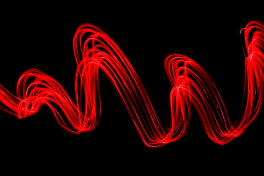 Long exposure photograph of neon red colour in an abstract swirl, parallel lines pattern against a black background. Light painting photography.